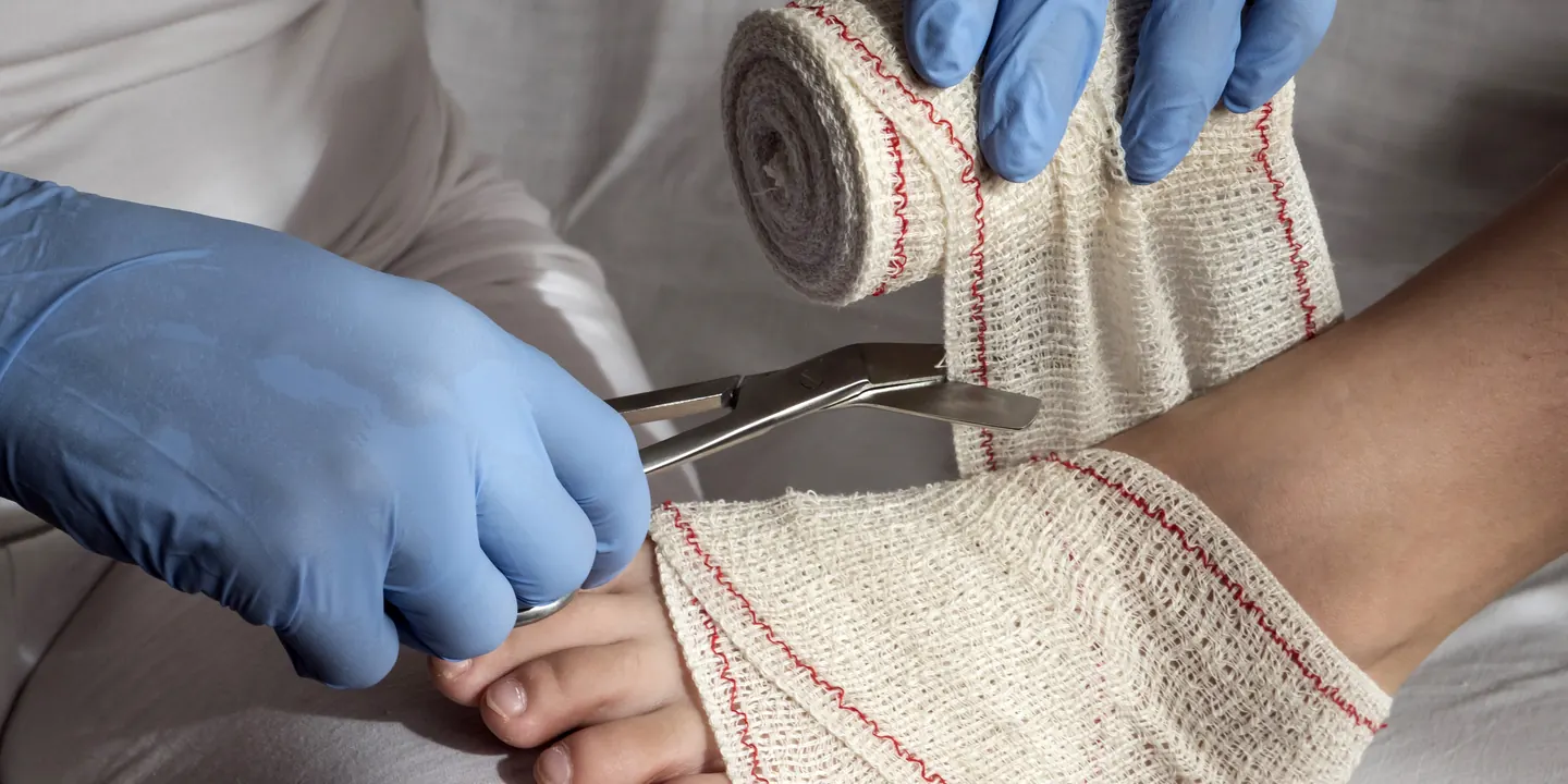 Gloved clinician applying a dressing to a foot during recovery from bunion surgery